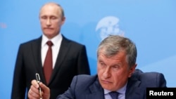 Russia's President Vladimir Putin (back) and Rosneft CEO Igor Sechin attend a signing ceremony at the St. Petersburg International Economic Forum 2014 in St. Petersburg, May 24, 2014.