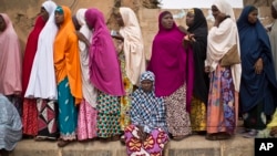 A tired Nigerian woman sits down to rest as others queue, while they face long delays to cast their vote in the afternoon at a polling station in Daura, the home town of opposition candidate Gen. Muhammadu Buhari, in northern Nigeria Saturday, March 28, 2015. Nigerians went to the polls Saturday in presidential elections which analysts say will be the most tightly contested in the history of Africa's richest nation and its largest democracy. (AP Photo/Ben Curtis)