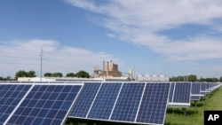 A solar panel array collects sunlight with the Fremont, Neb., power plant seen behind it, May 31, 2018. The Biden administration announced Monday that it would waive tariffs on solar panels imported to the United States from Cambodia, Malaysia, Thailand and Vietnam for 24 months.