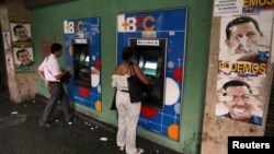 People withdraw money from cash machines where election propaganda supporting Venezuela's President Hugo Chavez cover the nearby walls in Caracas, February 8, 2013. 