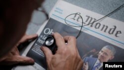 FILE - An employee checks a copy of the freshly-printed French daily evening newspaper Le Monde which announces the re-election of U.S. President Barack Obama, Paris, November 7, 2012. 