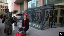 In this May 1, 2014, file photo, an Uighur woman rests near a cage protecting heavily armed Chinese paramilitary policemen on duty in Urumqi in China's northwestern region of Xinjiang. (AP Photo/Ng Han Guan, File)