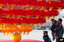 FILE - A man lifts a child up to lantern decorations setup ahead of the Chinese New Year in Beijing, China.