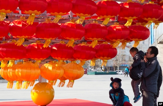 A man lifts a child up to lantern decorations setup ahead of the Chinese New Year in Beijing, China.