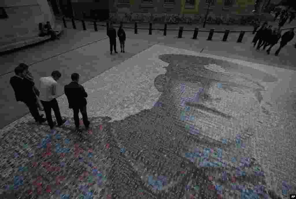 People walk on and around a digital mosaic of photographs of people, depicting British Army private James Ernest Beaney, killed during World War One, outside the BBC headquarters in central London.