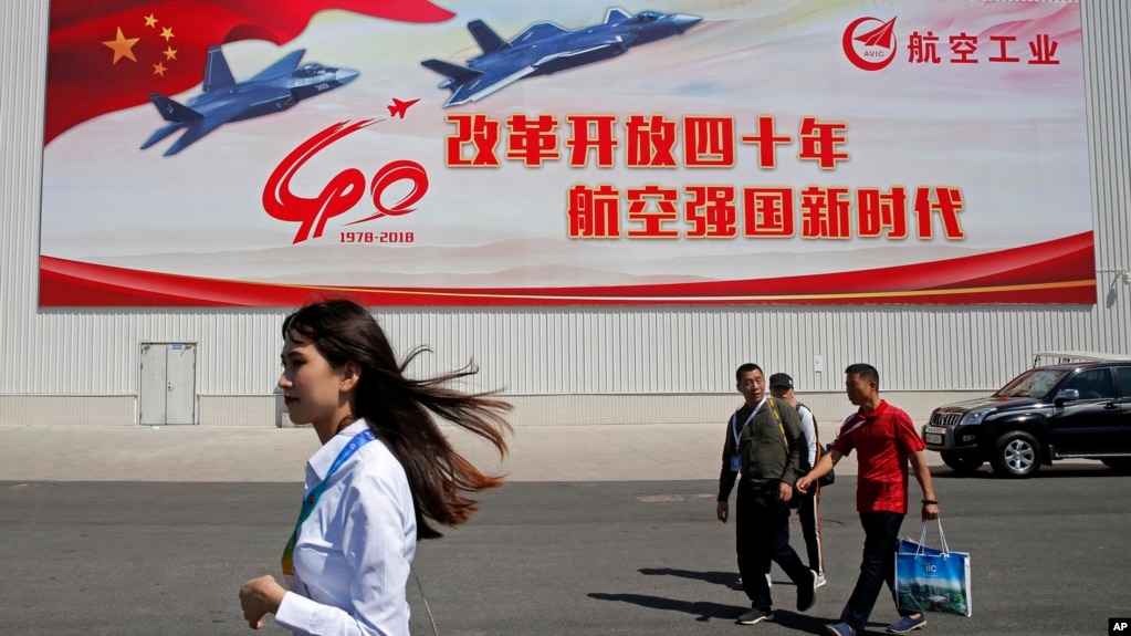 在广东珠海的第十二届中国国际航空航天展览会上，参观者走过中国喷气式战斗机的海报（2018年11月6日）。(photo:VOA)