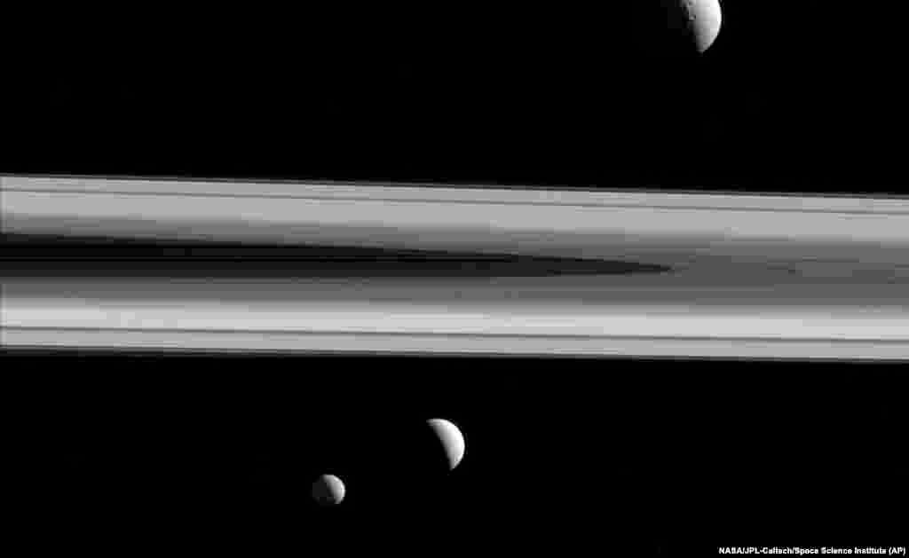 This Dec. 3, 2015 image made available by NASA shows three of Saturn's moons - Tethys, above, Enceladus, second left, and Mimas, seen from the Cassini spacecraft. 