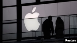 FILE - People walk past the Apple logo near an Apple Store at a shopping area in central Beijing, February 19, 2013.