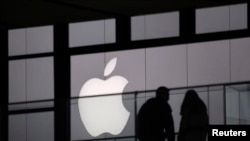 FILE - People walk past the Apple logo near an Apple Store at a shopping area in central Beijing.