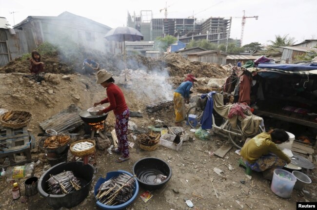 FILE - Women grills fish for sale at a slum area near railway tracks in Phnom Penh, Cambodia, Jan. 13, 2016.