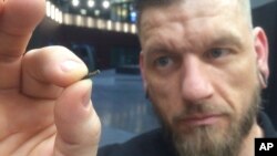 Jowan Osterlund from Biohax Sweden, holds a small microchip implant, similar to those implanted into workers at the Epicenter March 14, 2017. (AP Photo/James Brooks)