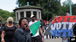 "El sistema estadounidense está manipulado": dice el letrero que alza una mujer mientras habla a manifestantes durante una manifestación en Brooklyn.