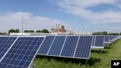 A solar panel array collects sunlight with the Fremont, Neb., power plant seen behind it, May 31, 2018. Solar energy is gaining traction in a small but growing number of Nebraska cities, but the technology still faces a number of obstacles that is keeping