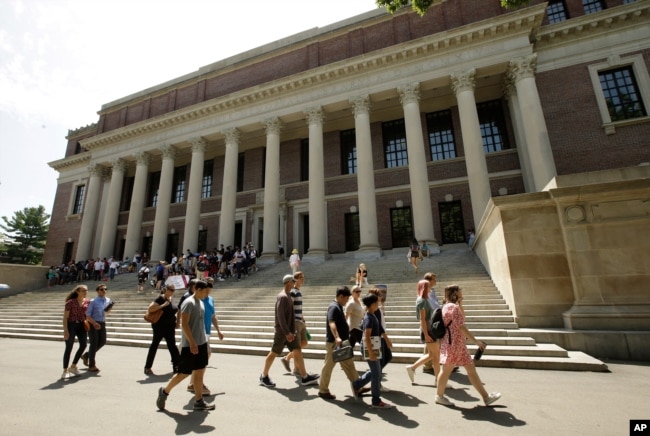 FILE - People walk past an entrance to Widener Library, behind, on the campus of Harvard University, in Cambridge, Mass., July 16, 2019.