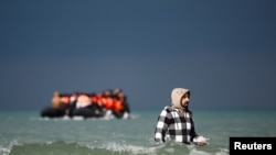 Seorang migran tampak memegang telepon genggam saat berupaya mendekati perahu balon yang akan bergerak menyeberangi Selat Inggris di pesisir Wimereux, Prancis, pada 4 September 2024. (Foto: Reuters/Benoit Tessier)