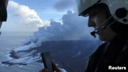Dr. Jessica Ball of USGS, a geologist and volcanologist who does research at the US Geological Survey, is updating Hawaiian Volcano Observatory scientists on the ground during a helicopter overflight of the ocean entry of the fissure 8 lava flow where a laze (lava haze) plume is visible over the active parts of the flow margin near Kapoho, Hawaii, June 8, 2018. 