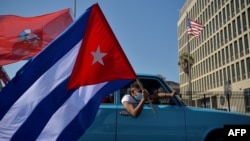 Cubanos pasan frente a la embajada de Estados Unidos durante una manifestación que pide el fin del bloqueo de Estados Unidos contra Cuba, en La Habana, 28 de marzo de 2021. [Foto de YAMIL LAGE / AFP]