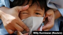 Seorang anak menggunakan masker pelindung ketika keluarganya berziarah menjelang bulan puasa Ramadhan, di tengah penyebaran corona (COVID-19), di Jakarta, 23 April 2020. (Foto: Reuters/Willy Kurniawan)