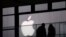 FILE - People walk past the Apple logo near an Apple Store at a shopping area in central Beijing.