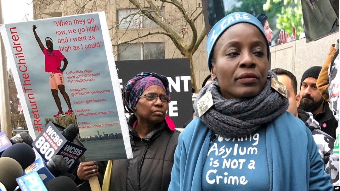 Therese Okoumou (kanan), yang memanjat dasar Patung Liberty pada 4 Juli untuk memprotes pemisahan keluarga migran di perbatasan Meksiko, berdiri di sebelah poster gambar dirinya di luar pengadilan Manhattan, 17 Desember 2018.
