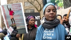 Therese Okoumou (kanan), yang memanjat dasar Patung Liberty pada 4 Juli untuk memprotes pemisahan keluarga migran di perbatasan Meksiko, berdiri di sebelah poster gambar dirinya di luar pengadilan Manhattan, 17 Desember 2018.
