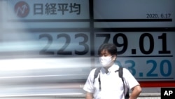 A man stands in front of an electronic stock board showing Japan's Nikkei 225 index at a securities firm as a vehicle goes by in Tokyo, June 17, 2020.