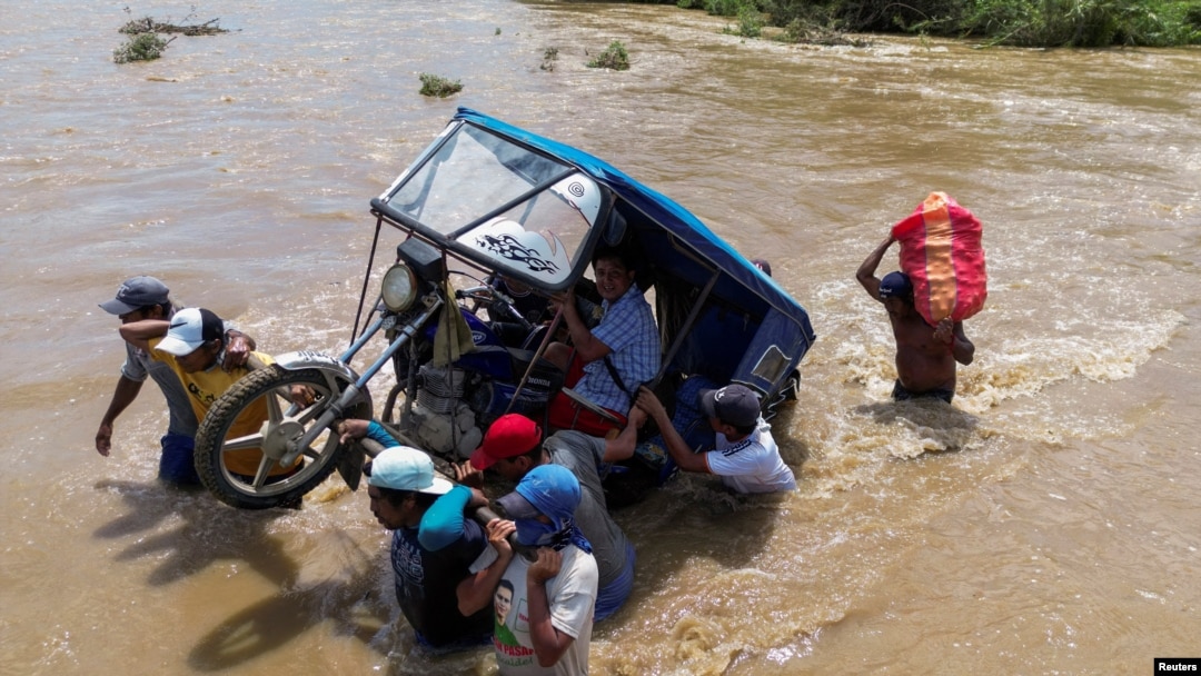 Un grupo de personas cargan un mototaxi por una corriente crecidas tras las lluvias provocadas por el ciclón Yaku en Piura, Perú, el 11 de marzo de 2023.