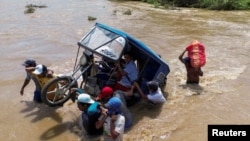 Un grupo de personas cargan un mototaxi por una corriente crecidas tras las lluvias provocadas por el ciclón Yaku en Piura, Perú, el 11 de marzo de 2023.