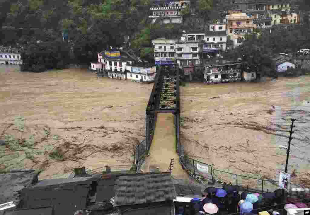 People gather to watch a bridge submerged in the flooded water of the River Ganges in Rudraprayag, in the northern Indian state of Uttarakhand, June 18, 2013.