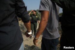 A U.S. border patrol agent stands next to men being detained after entering the United States by crossing the Rio Grande river from Mexico, in Roma, Texas, May 11, 2017.
