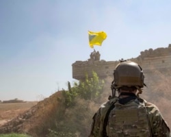 FILE - A U.S. soldier oversees members of the Syrian Democratic Forces as they demolish a Kurdish fighters' fortification and raise a Tal Abyad Military Council flag over the outpost as part of the "safe zone" near the Turkish border, Sept. 21, 2019.