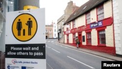 Papan berisikan pesan kesadaran jaga jarak di tengah pandemi COVID-19, terlihat di sisi jalan Buckingham, Inggris yang terlihat lengang, 23 February 2021. (REUTERS/Andrew Boyers)