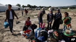 FILE - Syrian refugees wait with their belongings to leave a makeshift camp near the northern Greek village of Idomeni during a police operation at the Greek-Macedonian border, May 26, 2016. 
