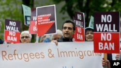 Protesters hold signs during a demonstration against President Donald Trump's revised travel ban, May 15, 2017, outside a federal courthouse in Seattle.