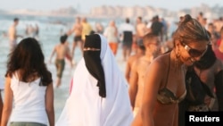 A woman wearing a bikini walks past a woman wearing a niqab on a beach in the Mediterranean city of Alexandria, about 220 km northwest of Cairo,Egypt, Aug. 7, 2009. 
