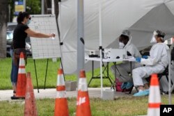 FILE - Health care workers take information from people in line at a walk-up COVID-19 testing site during the coronavirus pandemic, in Miami Beach, Florida, July 17, 2020.