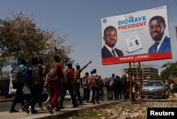 FILE—Students walks as they pass an electoral billboard of the Senegalese presidential candidate Bassirou Diomaye Faye in Dakar, Senegal, March 20, 2024.