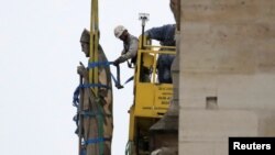 Men work on a statue on a facade at Notre-Dame Cathedral after a massive fire devastated large parts of the gothic structure in Paris, France, April 16, 2019.