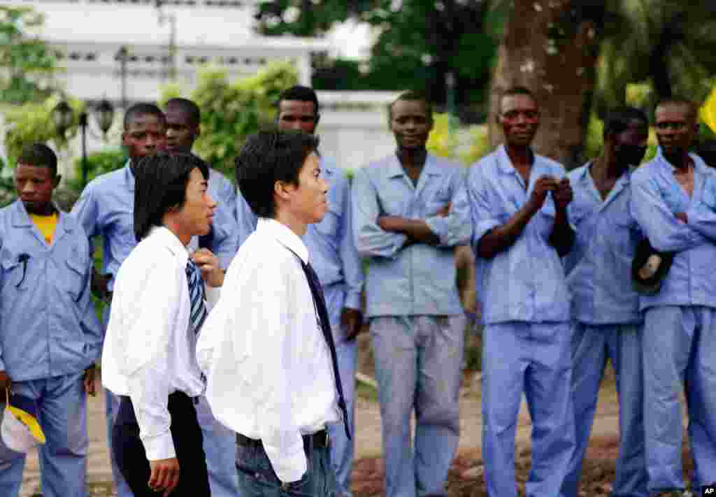 中国承包公司人员从刚果工人面前走过，他们正准备欢迎到访首都金莎萨的中国铁路工程总公司代表团（2010年3月29日）。该公司参加修建金莎萨的主要公路。中国为很多基础设施项目出资。