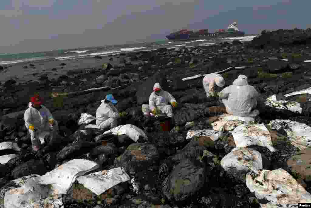 Workers remove oil during a clean-up operation after oil leaked from a cargo ship owned by TS Lines Co (in background), off the shores of New Taipei City, Taiwan, March 26, 2016.