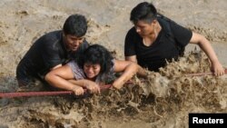 Rescuers help people cross a flooded street after a massive landslide and flood in the Huachipa district of Lima, Peru, March 17, 2017. 
