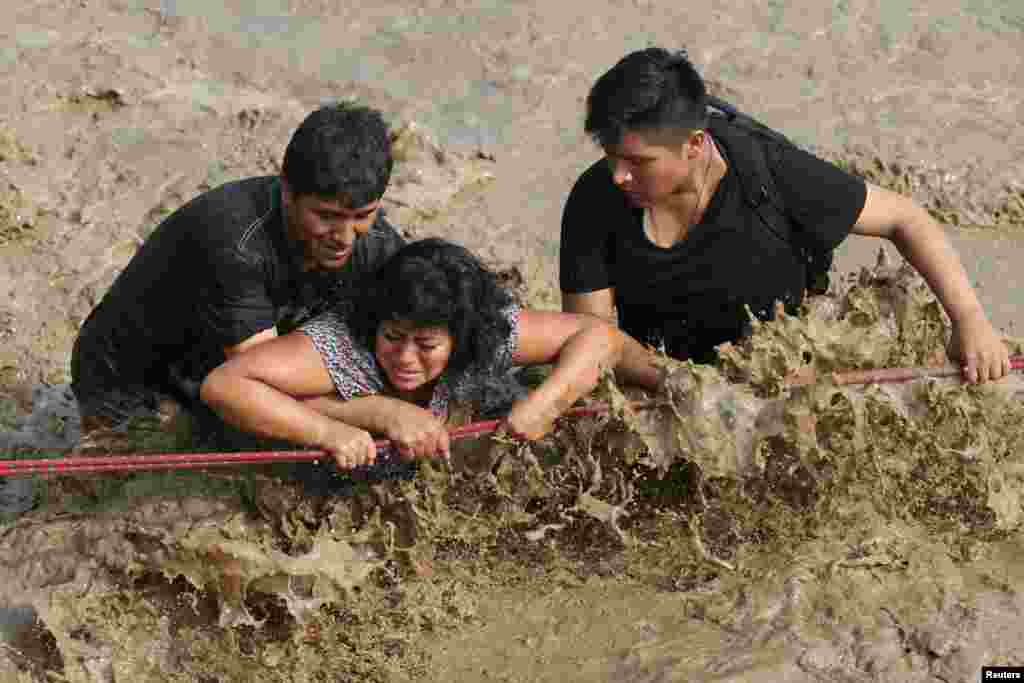 People hang on to a rescue line to cross a flooded street after a massive landslide and flood in the Huachipa district of Lima, Peru.