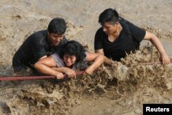 Rescuers help people cross a flooded street after a massive landslide and flood in the Huachipa district of Lima, Peru, March 17, 2017.