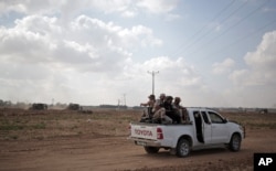 FILE - In this June 10, 2015 photo, Palestinian Hamas gunmen ride on the back of a pick-up truck as they patrol the border with Israel near the southern Gaza Strip town of Khan Younis, as Israeli military bulldozers are seen in the background.
