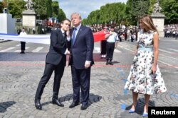 FILE - French President Emmanuel Macron, left, shakes hands with U.S. President Donald Trump, next to U.S. first lady Melania Trump during the traditional Bastille Day military parade on the Champs-Elysees in Paris, July 14, 2017.