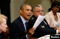 FILE - U.S. President Barack Obama holds up a copy of the report by the Task Force on 21st Century Policing at the White House in Washington, March 2, 2015. Beside Obama at right is Philadelphia Police Commissioner Charles Ramsey.