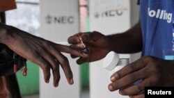 A National Elections Commission official puts indelible ink on the finger of a voter at a polling station during a runoff election between Liberian President George Weah and former Vice President Joseph Boakai, in Monrovia, Liberia, on Nov. 14, 2023.