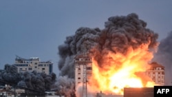 Ljudi stoje na krovu i gledaju kako se kugla vatre i dima diže iznad zgrade u gradu Gaza 7. oktobra 2023. tokom izraelskog zračnog napada.