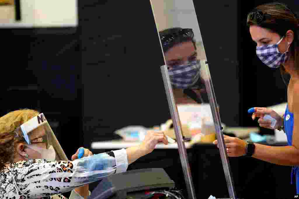 Harris County election clerk Nora Martinez, left, helps a voter in the Texas primary runoffs in Houston.