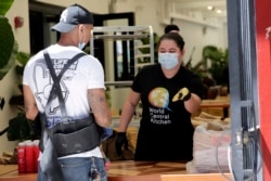 Volunteer Karla Hoyos hands out meals from the Red Rooster Overtown restaurant during the new coronavirus pandemic in Miami, March 30, 2020. Chef Marcus Samuelsson loaned his as-yet-unopened Red Rooster Overtown restaurant to chef Jose Andres' staff